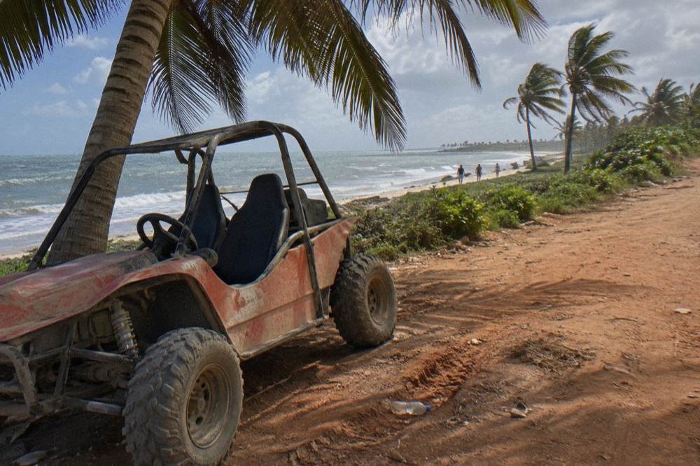 Two-seater dune buggy parked on a dirt trail beside palm trees