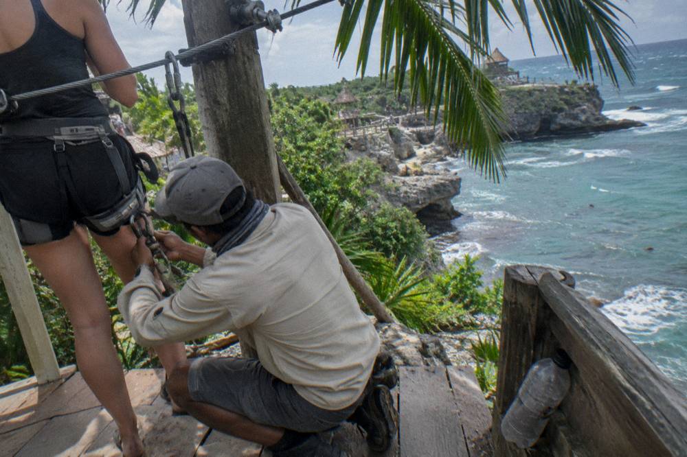 Guide checking a safety harness buckle on a rider at a forest platform