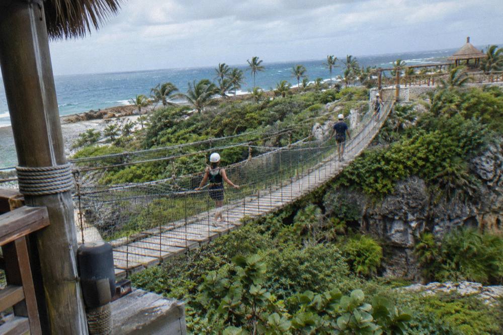 Group of riders in helmets walking a raised wooden walkway between forest platforms