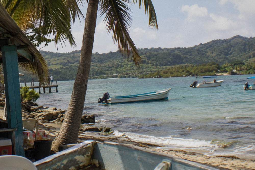 A calm turquoise bay surrounded by green hills with small boats anchored offshore