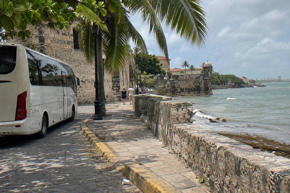 A touring coach parked on a shaded street beside old stone walls