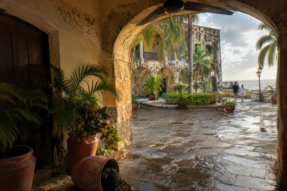 A stone archway opening onto a bright colonial courtyard with potted plants