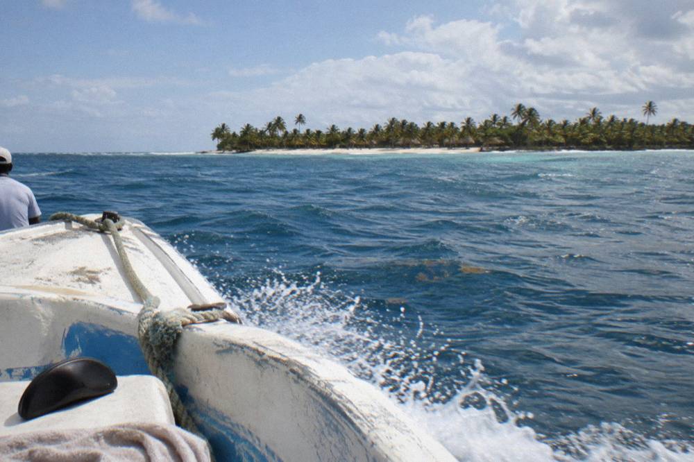 A speedboat crossing open blue water toward a distant island coastline