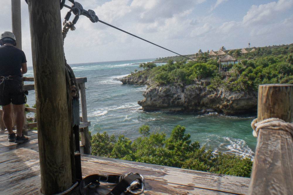 A steel cable zipline stretching between wooden platforms high in a green forest canopy