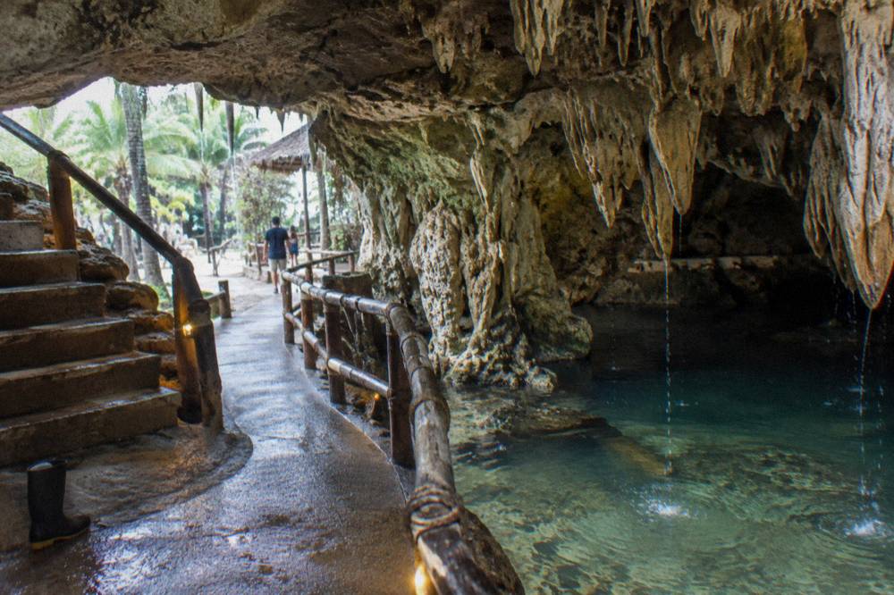 A limestone cave interior with a lit walkway and stalactites overhead