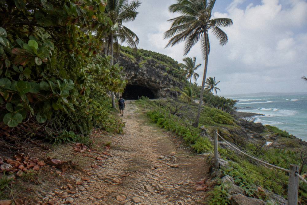 A country road through green farmland leading toward a limestone cave entrance