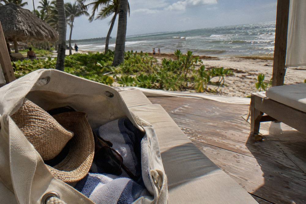 Open beach bag on a sunlit deck chair with a towel, hat and sunglasses packed for a boat day