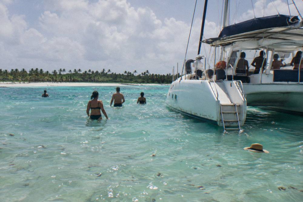 Catamaran anchored over a shallow turquoise sandbar with passengers wading in waist-deep water