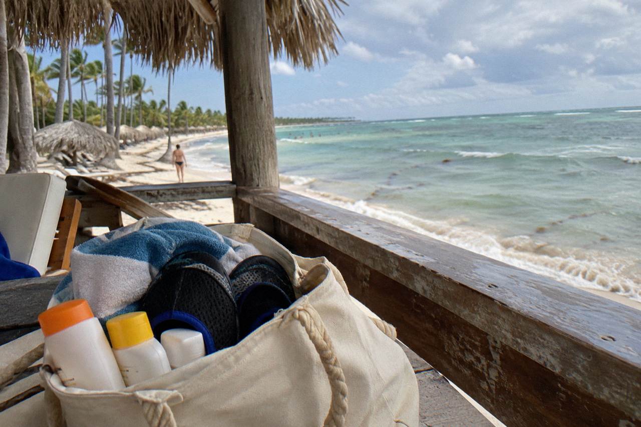 Beach bag with sunscreen, water shoes and towels on a wooden deck overlooking a calm Caribbean sea